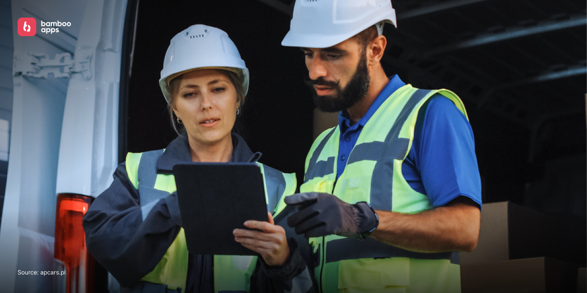 Two logistics workers in safety gear checking a tablet in front of a van